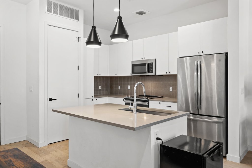 800 Embassy Drive, Unit 413 Austin, TX 78702 - Photo 2 of 27 Kitchen with stainless steel appliances, a kitchen island with sink, white cabinets, and light wood-style floors