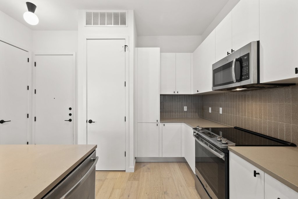 800 Embassy Drive, Unit 413 Austin, TX 78702 - Photo 6 of 27 Kitchen with stainless steel appliances, light wood-style floors, white cabinets, and tasteful backsplash