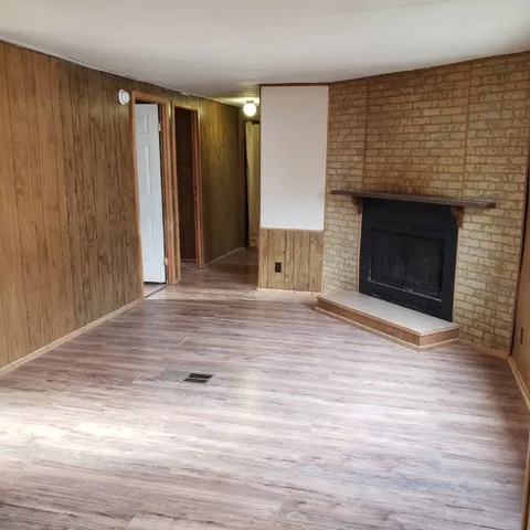 an empty room with wooden floor fireplace and windows