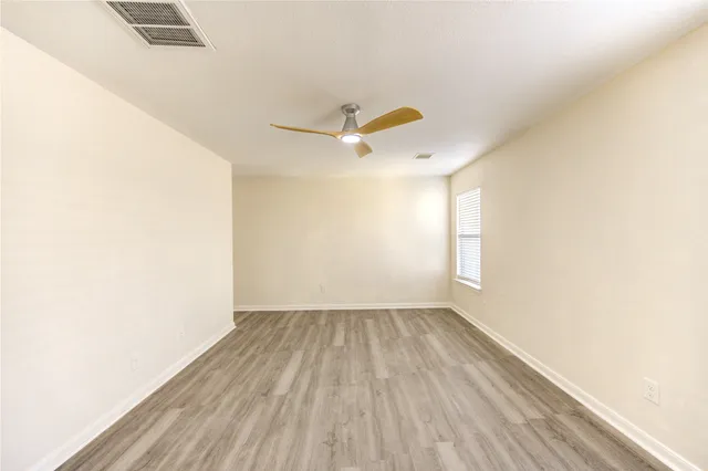 an empty room with wooden floor fan and windows