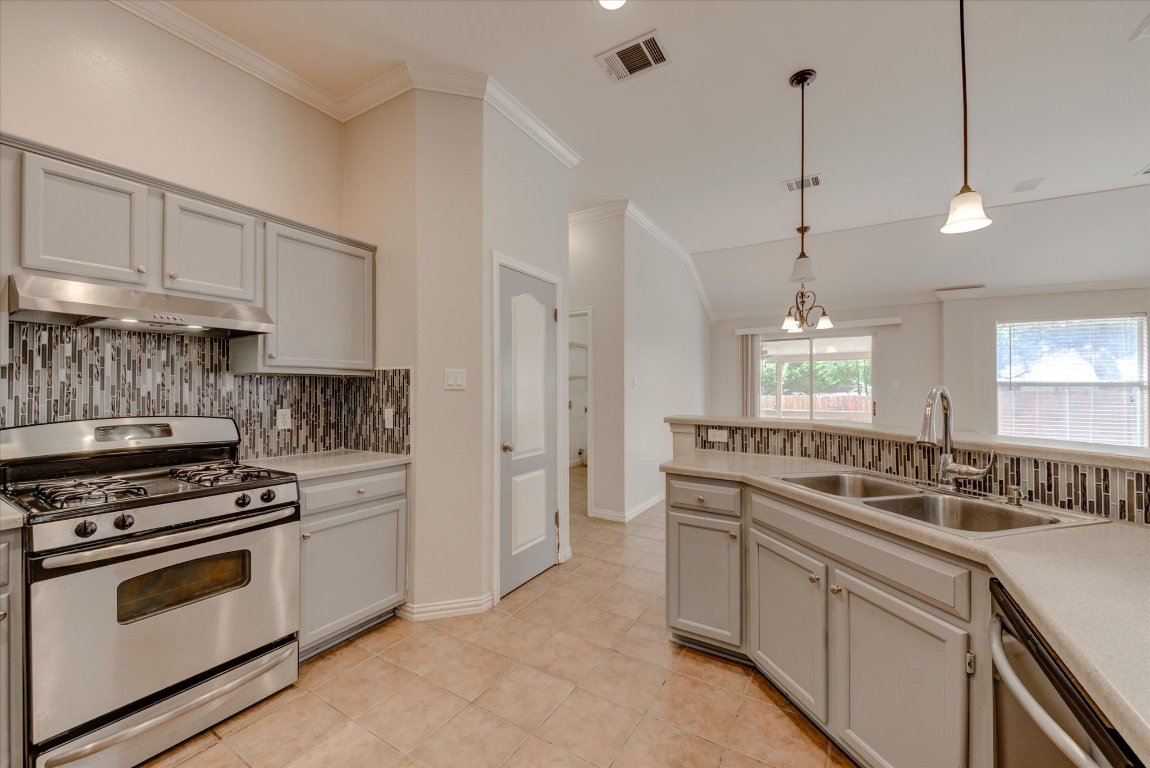 Kitchen with stainless steel appliances, ornamental molding, backsplash, decorative light fixtures, and light countertops