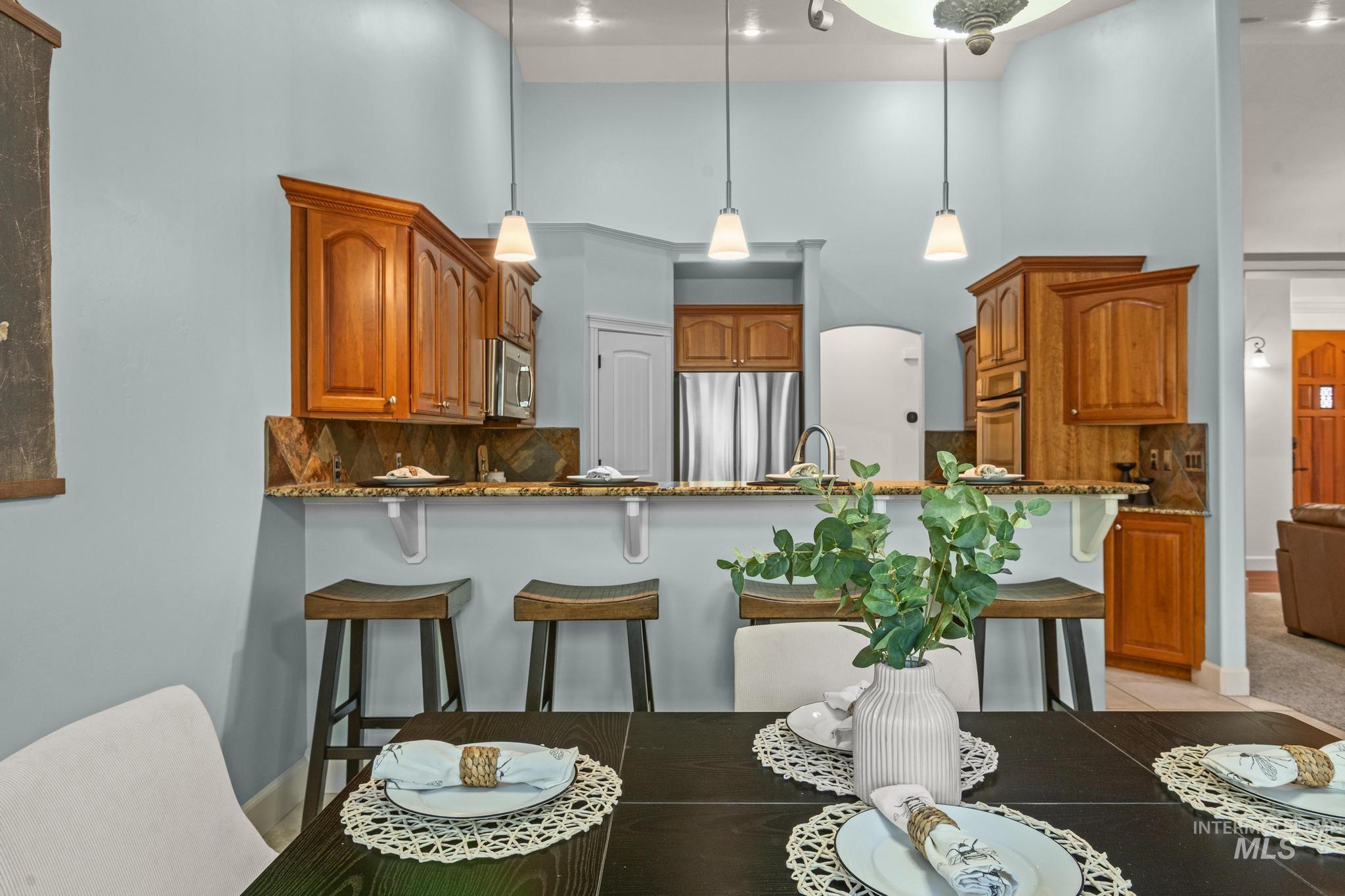 4946 North Villa Ridge Way Boise, ID 83703 - Photo 16 of 49 Kitchen bar seating area featuring an integrated stainless steel sink, granite countertops, wood cabinetry, and pendant lighting