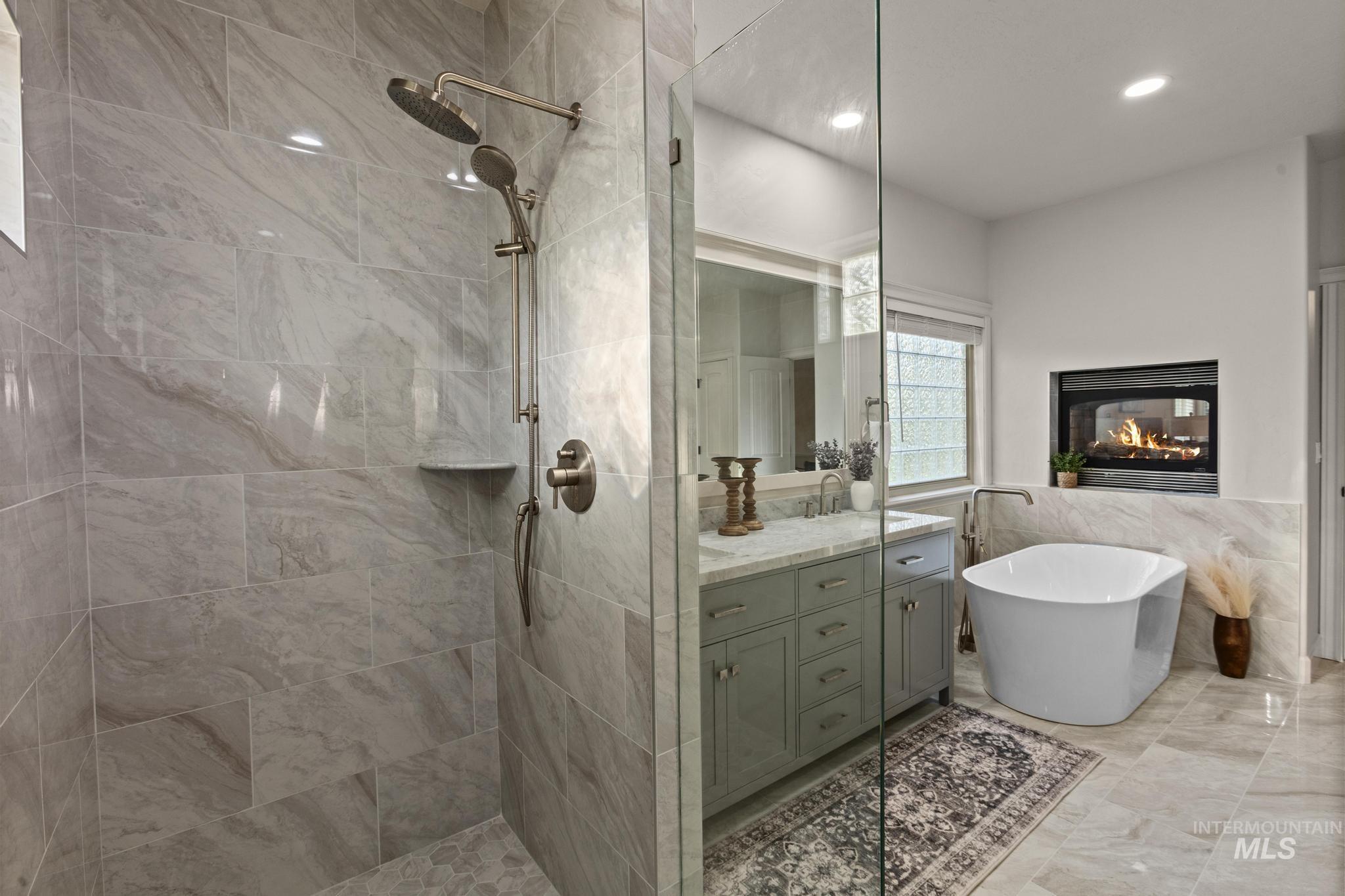 4946 North Villa Ridge Way Boise, ID 83703 - Photo 23 of 49 Contemporary bathroom featuring a spacious glass-enclosed shower with dual showerheads, a freestanding soaking tub, a built-in fireplace, a single vanity with stone countertops, and large format tile flooring