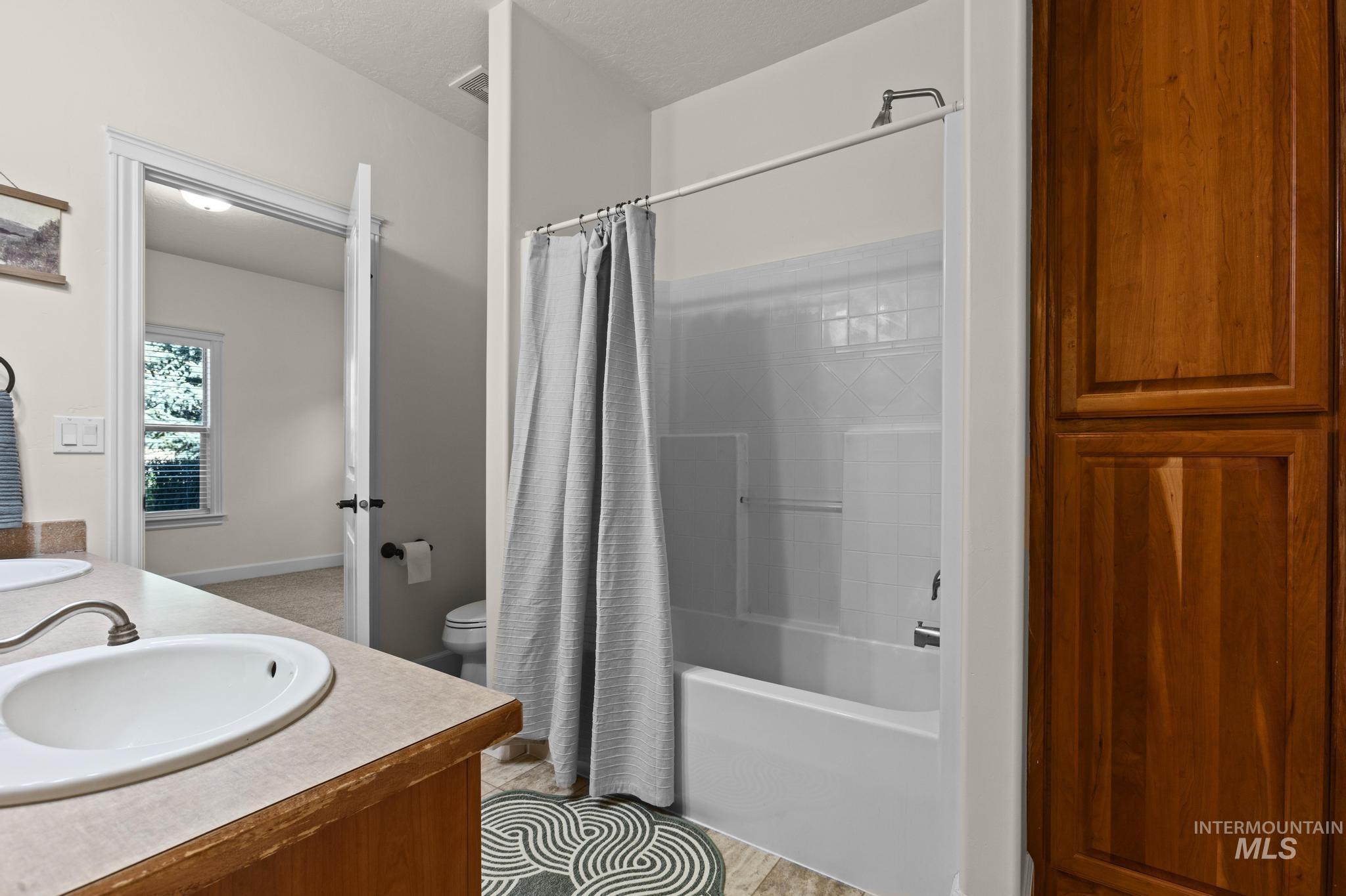 4946 North Villa Ridge Way Boise, ID 83703 - Photo 33 of 49 Bathroom featuring a white tub and shower combination with a tile surround, a built-in wood-finish storage cabinet, a vanity with an integrated sink and light-colored countertop, and wood-finish flooring