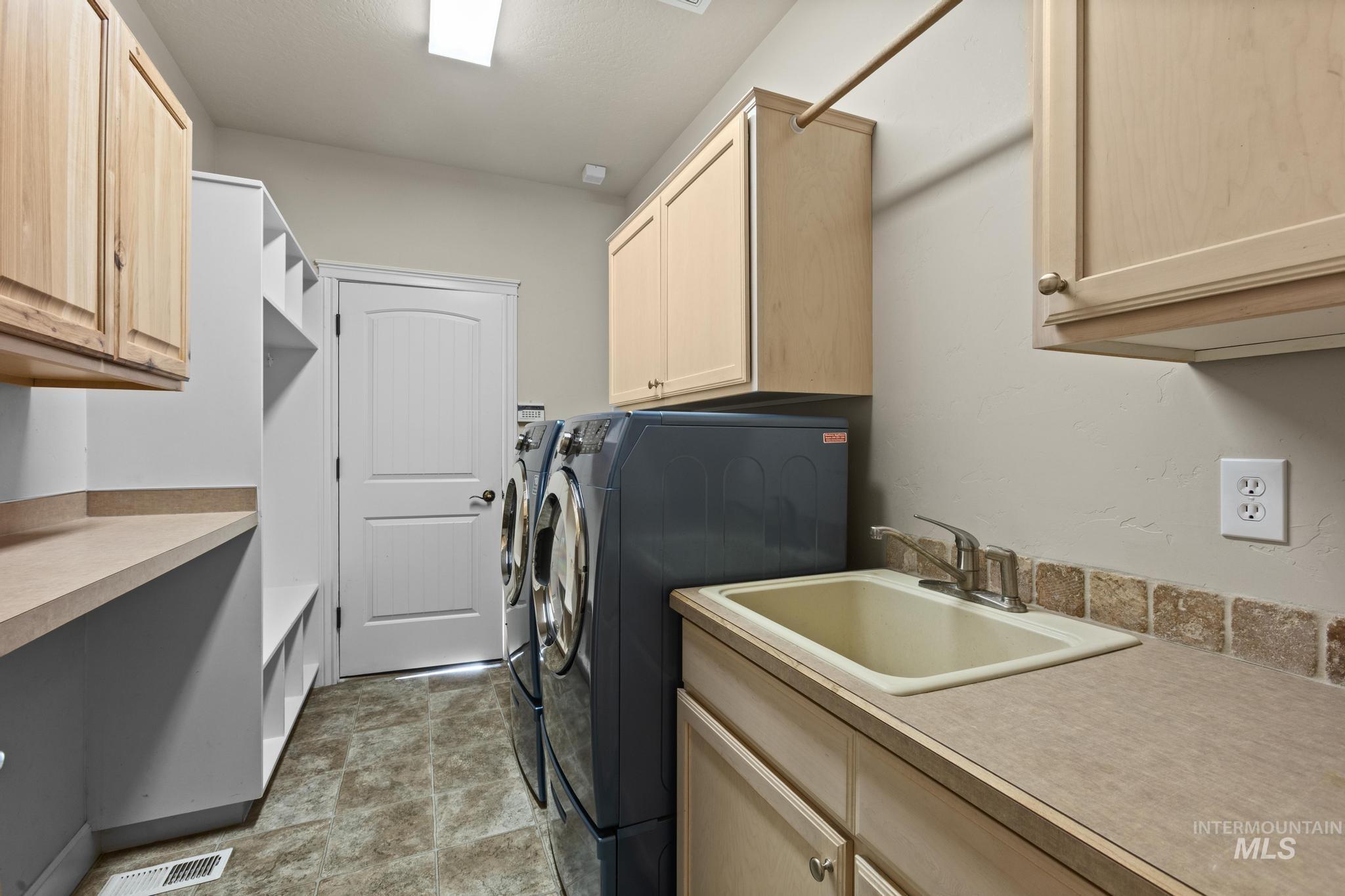 4946 North Villa Ridge Way Boise, ID 83703 - Photo 37 of 49 Utility room featuring built-in shelving, light wood-finish cabinetry, a utility sink with a chrome faucet, and a stone-look tile backsplash