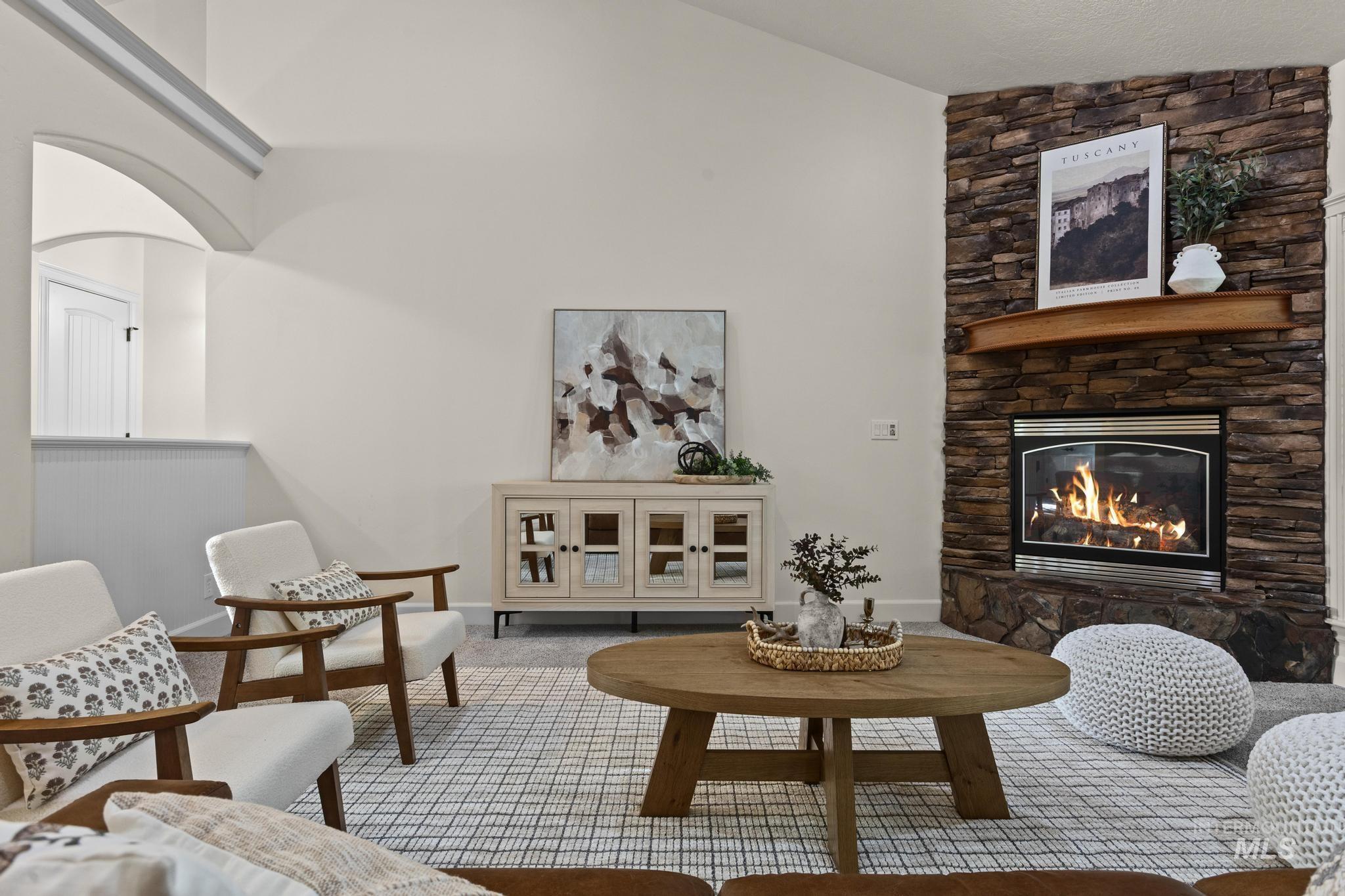4946 North Villa Ridge Way Boise, ID 83703 - Photo 7 of 49 Living area featuring a stone-clad fireplace with a wood mantel, vaulted ceilings, and an arched architectural opening