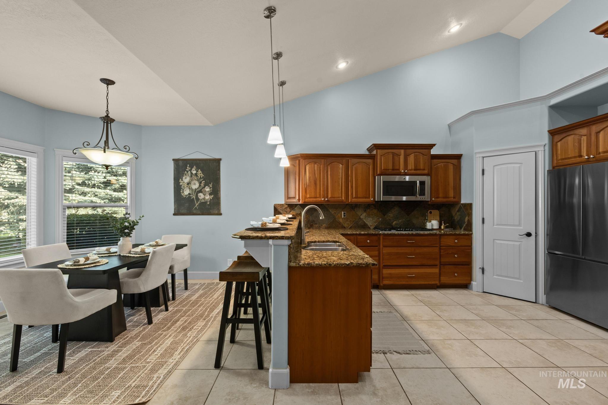 4946 North Villa Ridge Way Boise, ID 83703 - Photo 10 of 49 Kitchen and dining area featuring vaulted ceilings, light wood cabinetry, stone countertops, and a tiled backsplash