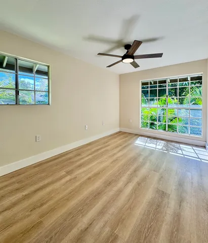 a view of an empty room with wooden floor and fan