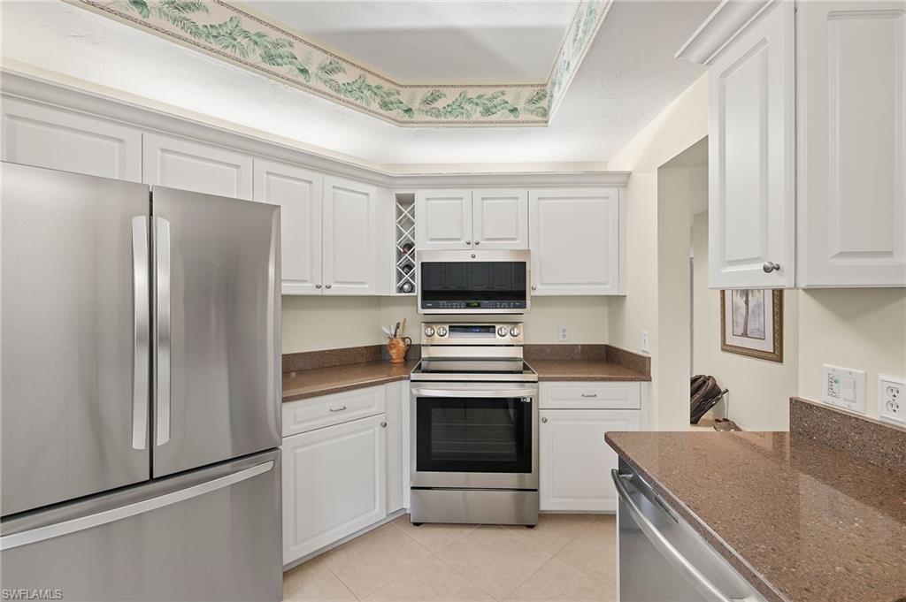 6500 Valen Way, Unit A203 Naples, FL 34108 - Photo 4 of 18 Kitchen featuring light tile patterned flooring, appliances with stainless steel finishes, white cabinetry, and dark stone counters