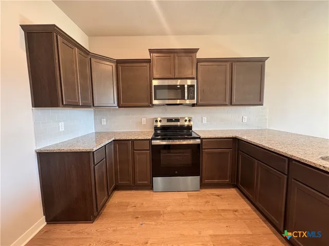 a kitchen with stainless steel appliances granite countertop a stove a sink dishwasher and a microwave oven on the wooden cabinets