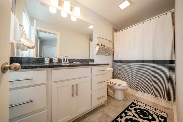 a bathroom with a granite countertop sink a toilet a mirror and vanity
