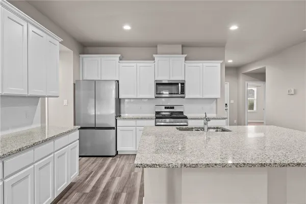 a kitchen with kitchen island granite countertop a sink a stove a refrigerator and white cabinets