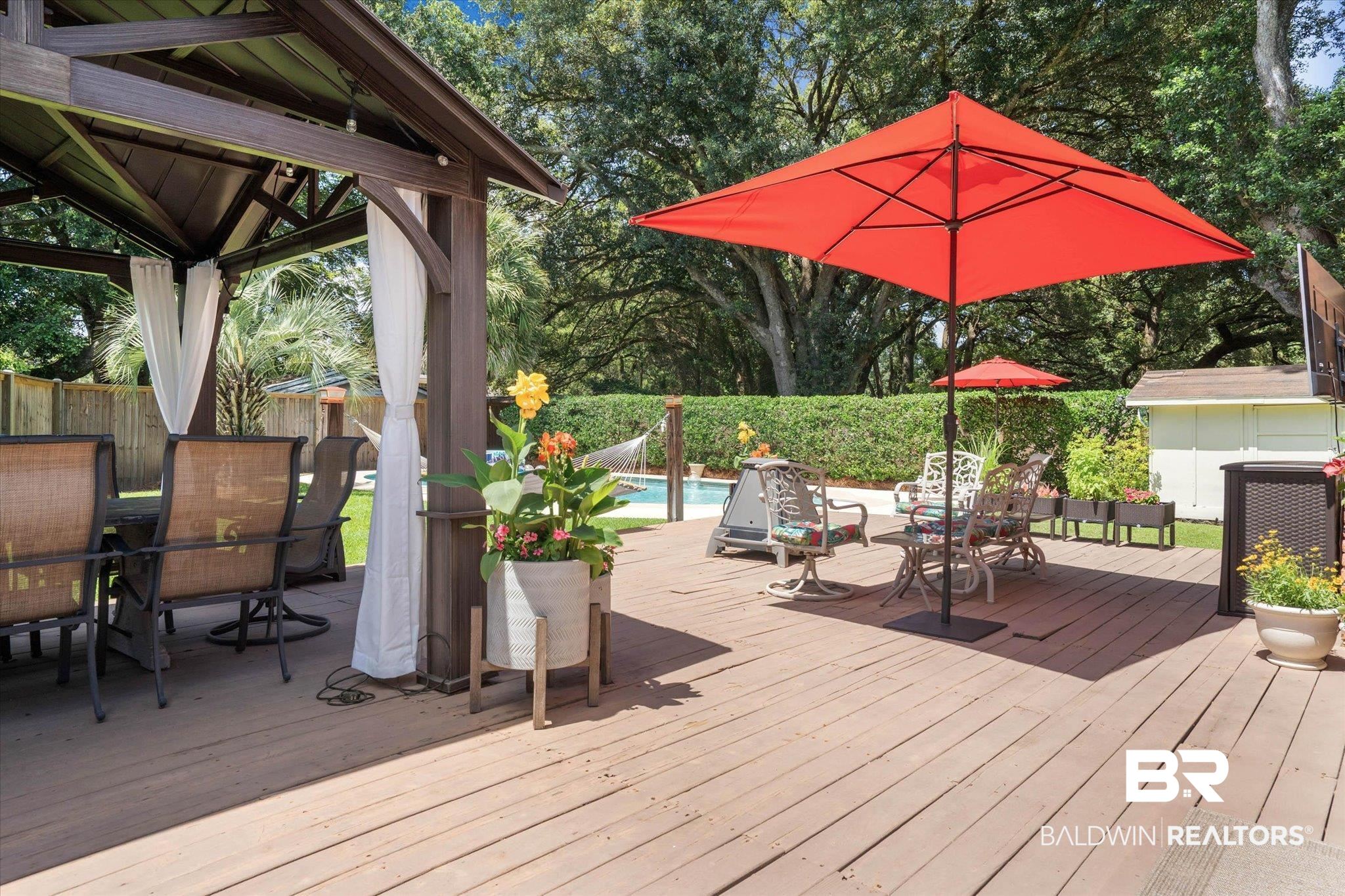 101 Ann Street Daphne, AL 36527 - Photo 25 of 38 Expansive outdoor decking featuring a wood-toned surface, a built-in gazebo with draped privacy screens, and a clear-water swimming pool