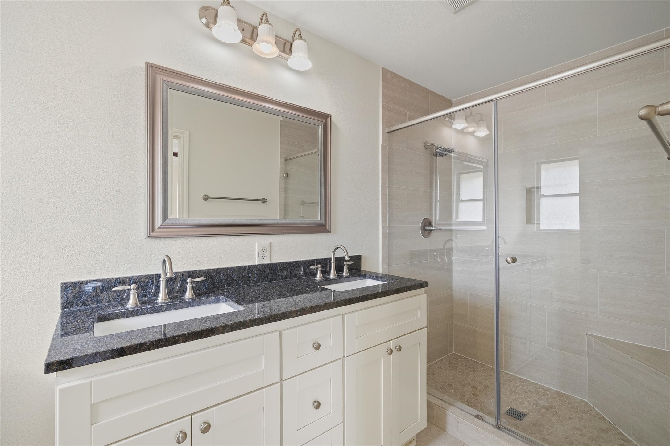 3331 Arbor Street Houston, TX 77004 - Photo 24 of 30 This bathroom features a modern double-sink vanity with a sleek granite countertop, a large mirror, and stylish lighting. It includes a spacious glass-enclosed shower with elegant tiling.