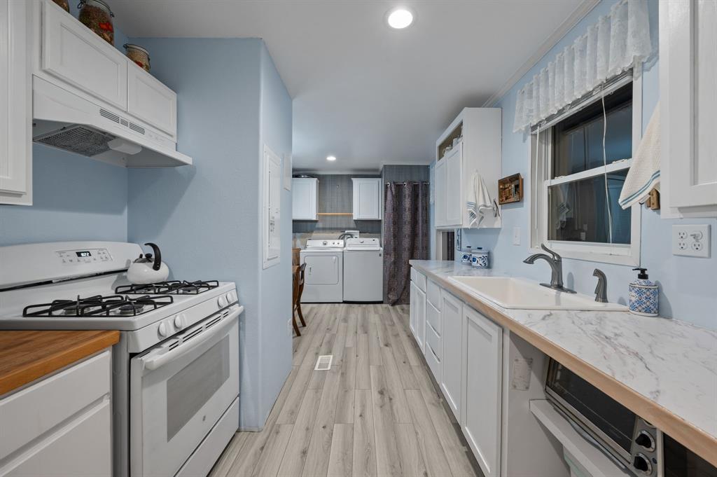 10902 Clear Creek Road West Sanger, TX 76266 - Photo 31 of 40 2nd House Kitchen with white gas range oven, white cabinets, washing machine and clothes dryer, under cabinet range hood, and light countertops