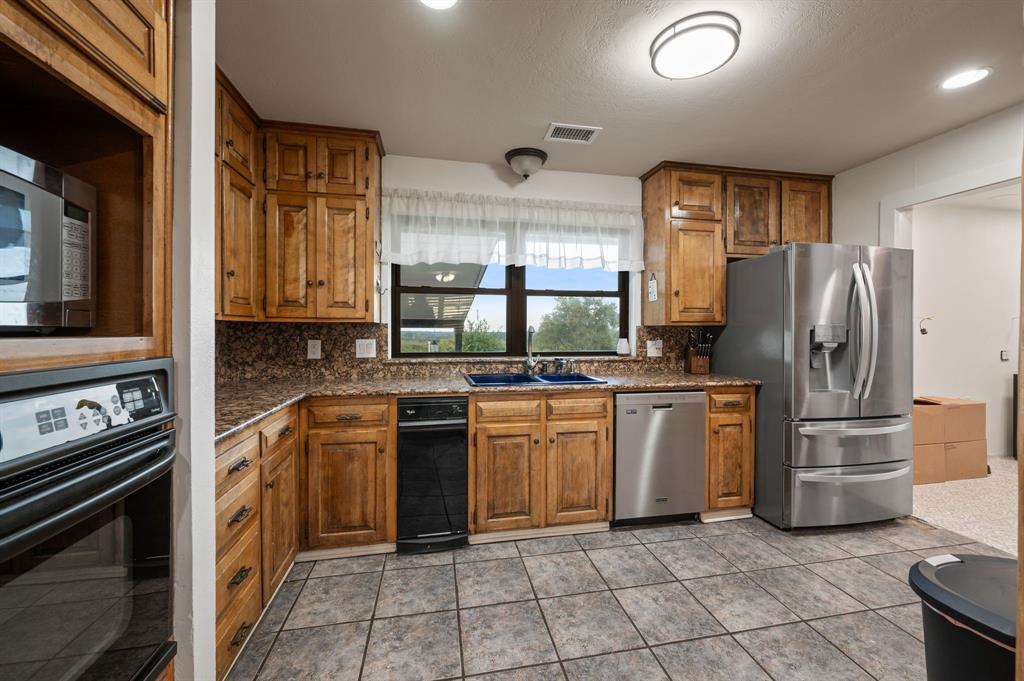 10902 Clear Creek Road West Sanger, TX 76266 - Photo 6 of 40 Kitchen featuring appliances with stainless steel finishes, brown cabinetry, backsplash, dark stone counters, and recessed lighting