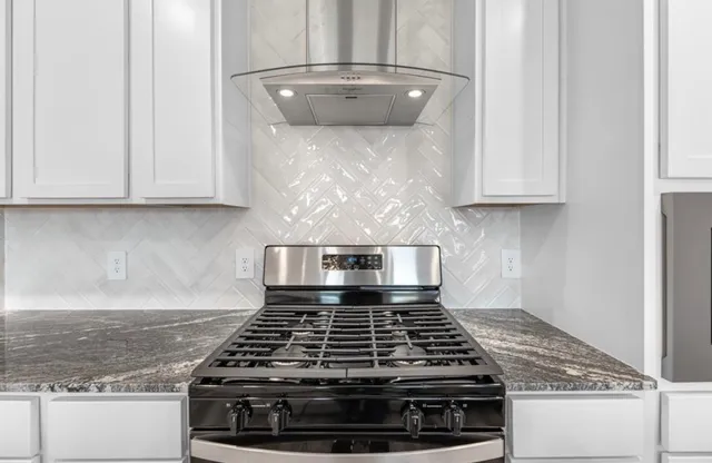 a kitchen with granite countertop a stove and white cabinets