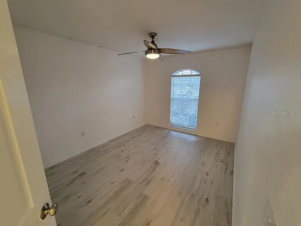 an empty room with wooden floor ceiling fan and window