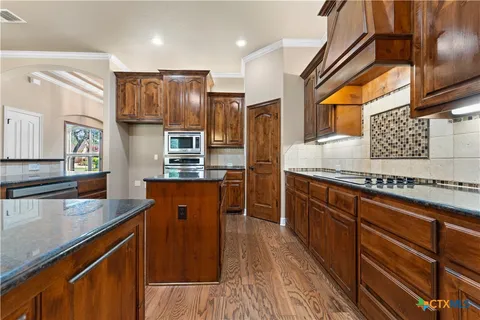 a kitchen with stainless steel appliances granite countertop a refrigerator a sink dishwasher a stove and white countertops with wooden floor