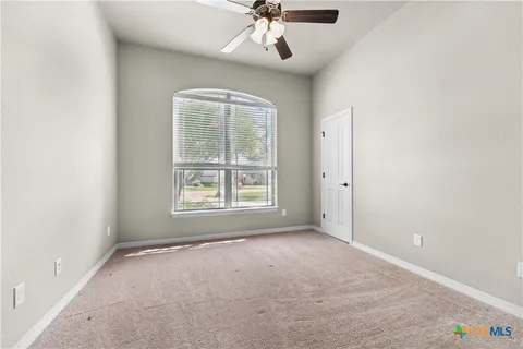 an empty room with a chandelier fan and windows