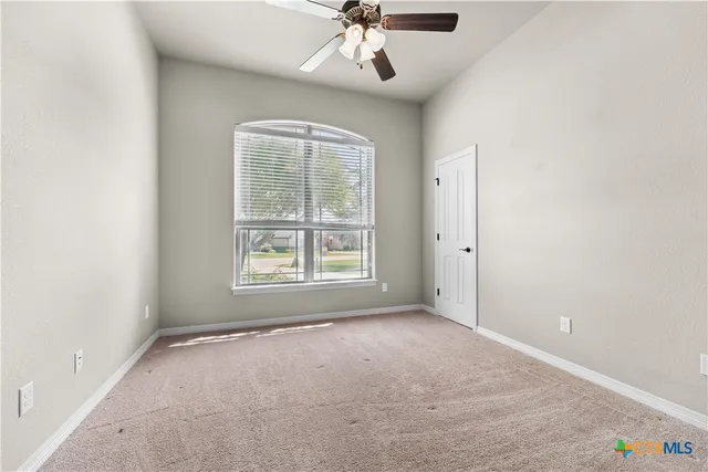 an empty room with a chandelier fan and windows