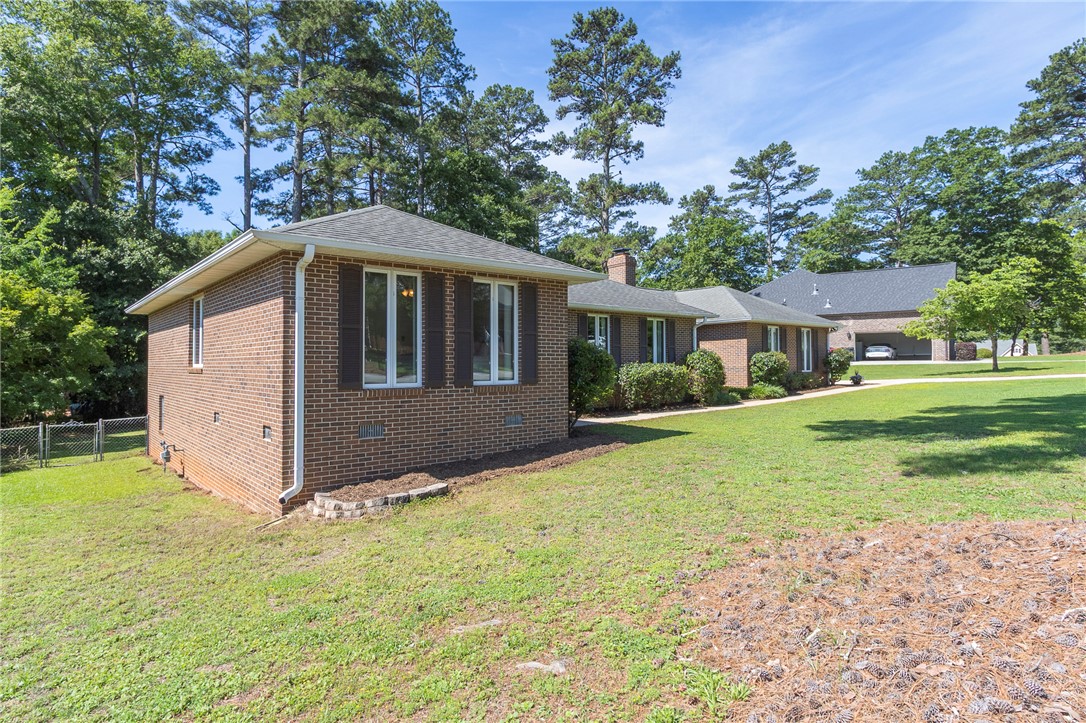 207 Laurel Ridge Road Anderson, SC 29621 - Photo 2 of 50 Mature trees frame a charming brick residence with a neatly manicured lawn, offering a serene outdoor setting.