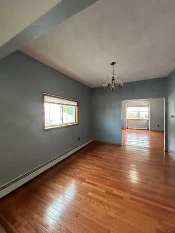 an empty room with wooden floor chandelier and windows