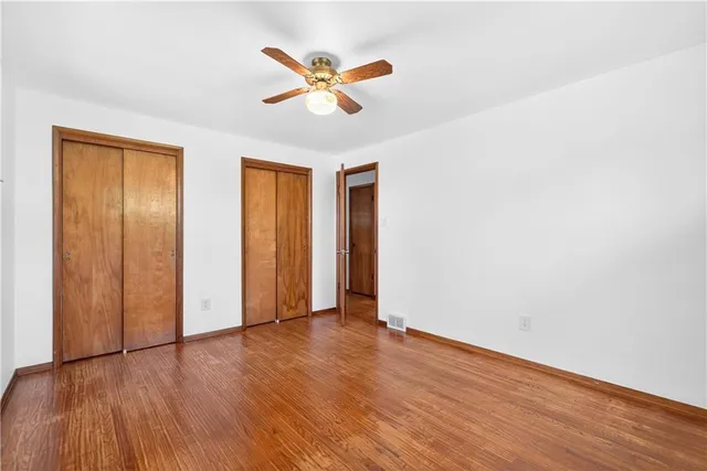 an empty room with wooden floor ceiling fan and windows