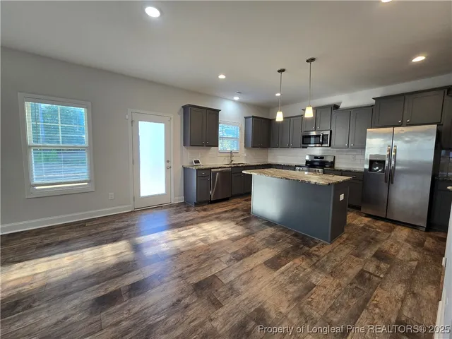 a kitchen with stainless steel appliances granite countertop a refrigerator a sink dishwasher a stove top oven a refrigerator and island with wooden floor