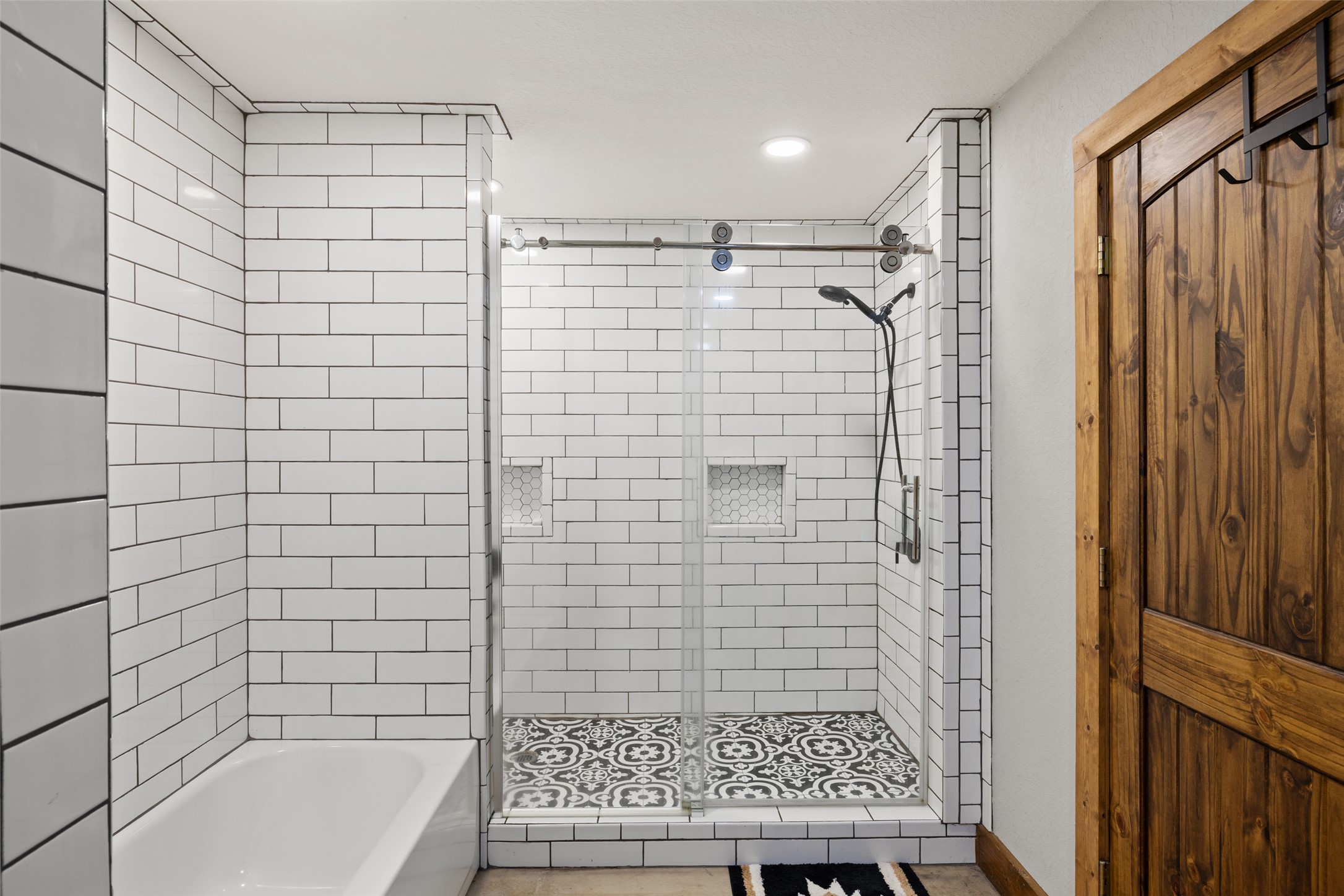 664 Martindale Falls Road Martindale, TX 78655 - Photo 13 of 21 Bathtub and shower combination featuring white subway tile surround, clear glass shower enclosure with sliding hardware, built-in shower niches, and patterned floor tile in the shower base