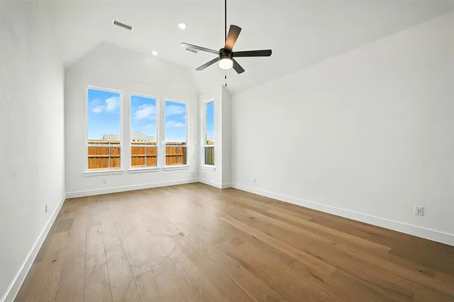 an empty room with wooden floor ceiling fan and windows