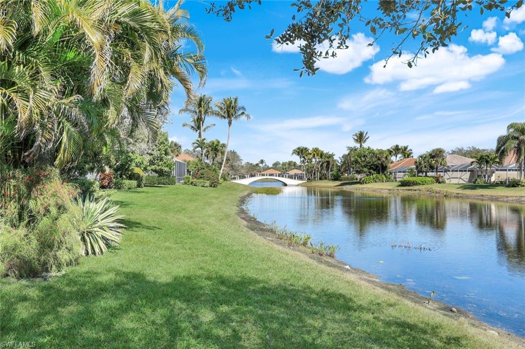 3108 Dominica Way Naples, FL 34119 - Photo 21 of 39 Waterfront property featuring a landscaped lawn, mature palm trees, and a decorative bridge across the water