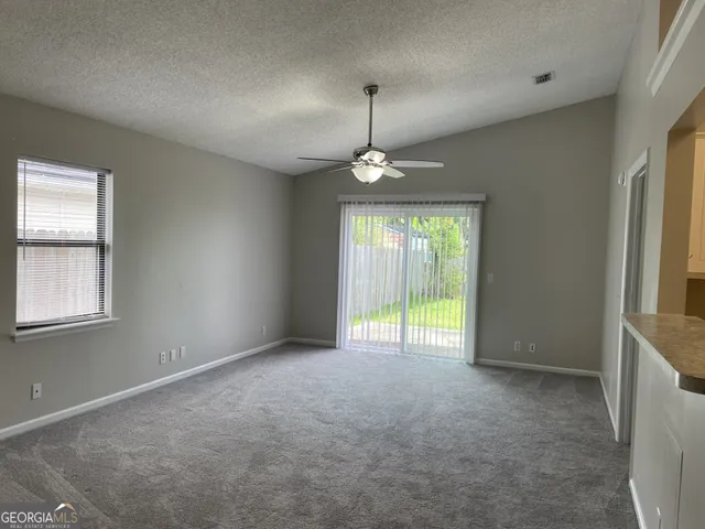 an empty room with chandelier fan and windows