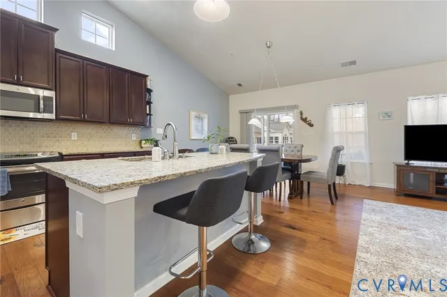 a open kitchen with stainless steel appliances granite countertop a stove top oven a sink a dining table and chairs with wooden floor