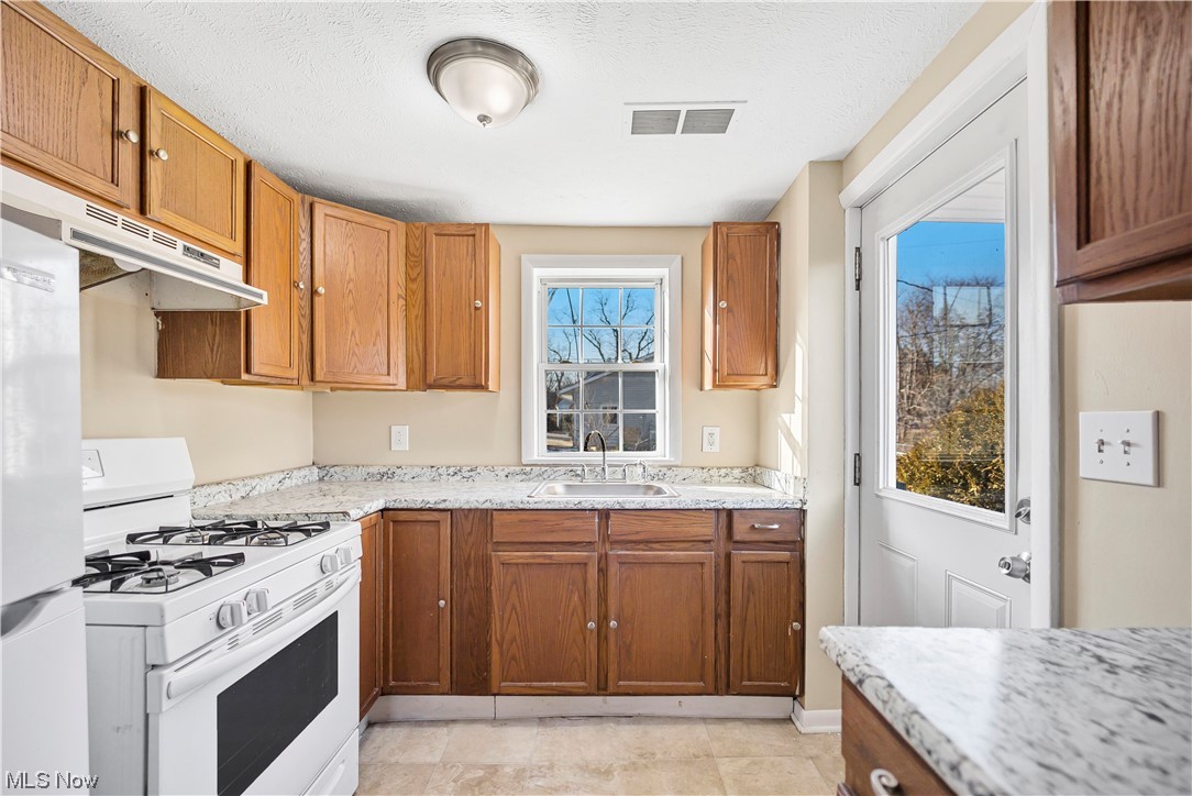 Kitchen featuring white appliances, light tile floors, light counters, and sink
