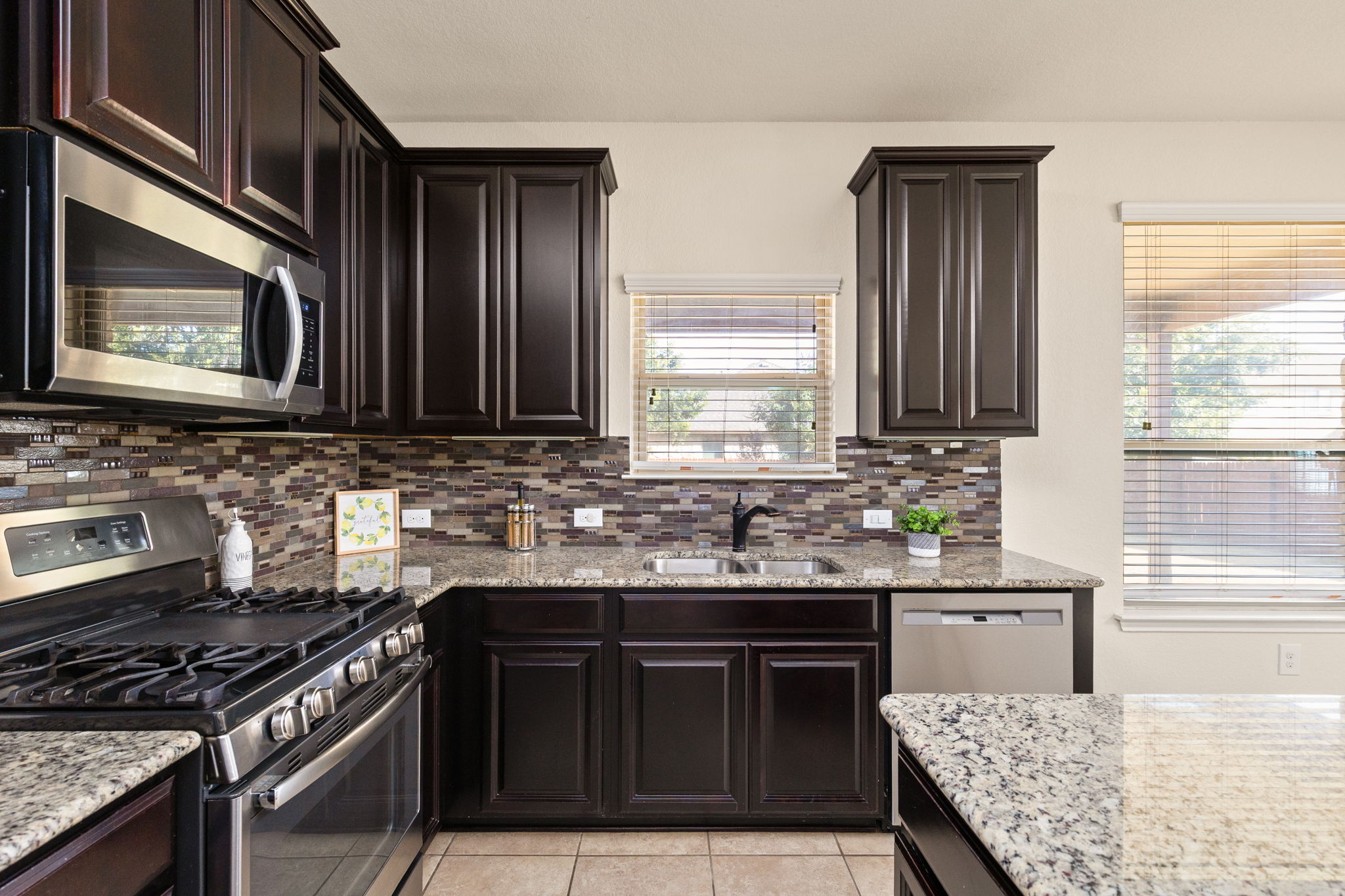 2400 Leonards Pass Leander, TX 78641 - Photo 18 of 40 A well-appointed kitchen features dark wood cabinetry, granite counters, and a sleek tiled backsplash.