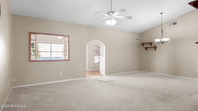 an empty room with a chandelier fan and windows