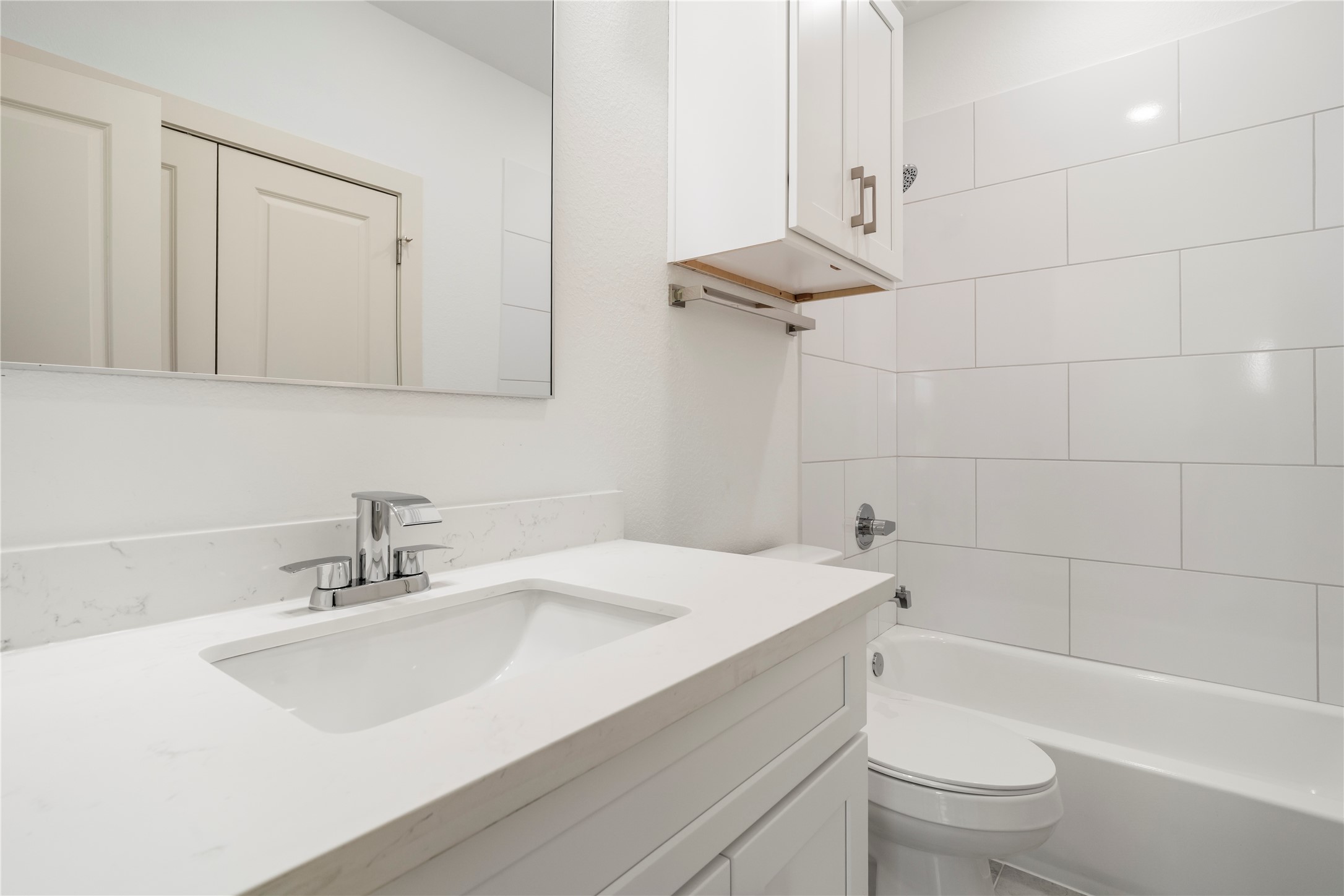 5629 Malmedy Road Houston, TX 77033 - Photo 23 of 24 Sleek and modern bathroom featuring a spacious vanity with a white countertop, elegant fixtures, and a pristine tub-shower combo with stylish white tile accents.