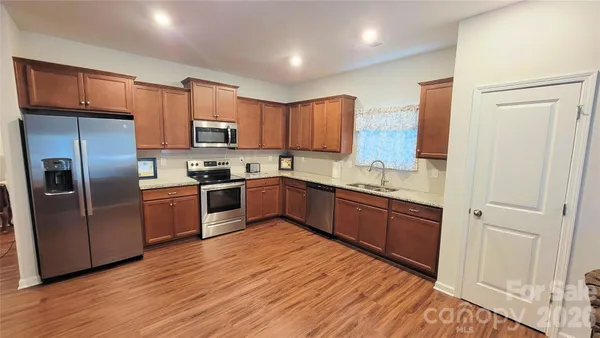 a kitchen with stainless steel appliances granite countertop a refrigerator a sink dishwasher a stove with wooden floors and cabinets
