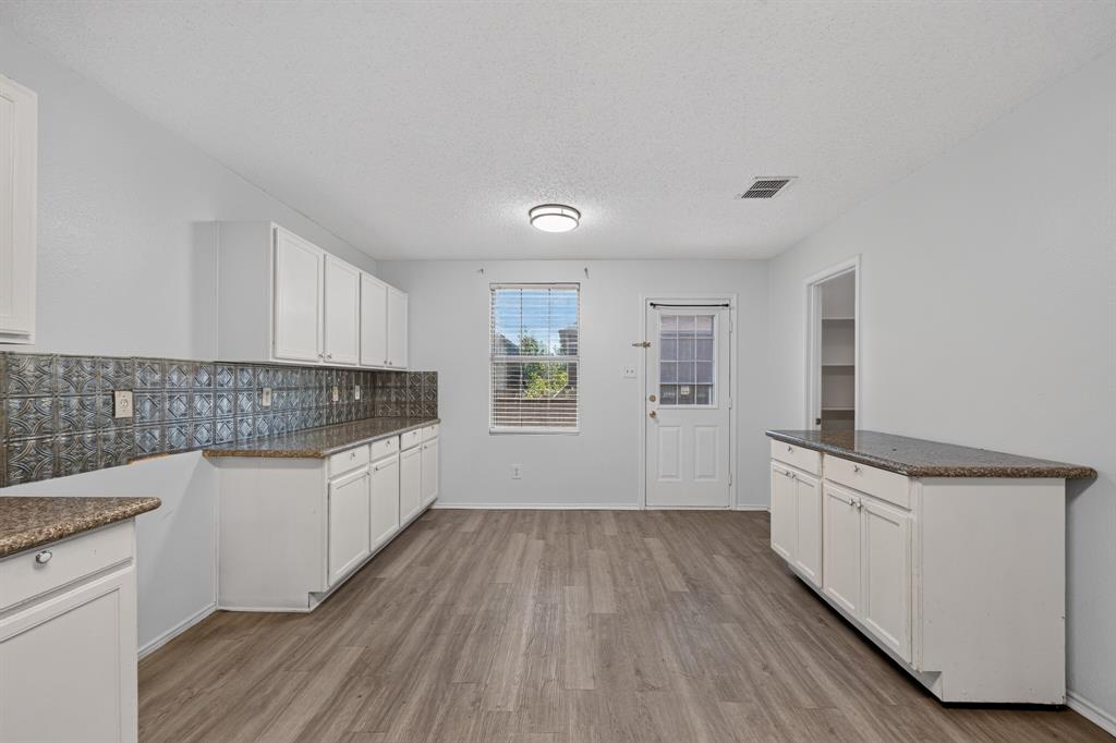 5416 Temecula Road Fort Worth, TX 76244 - Photo 6 of 27 Spacious kitchen featuring extensive white cabinetry, speckled countertops, wood-finish flooring, a decorative tile backsplash, and ample natural light