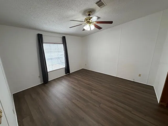an empty room with wooden floor chandelier fan and windows