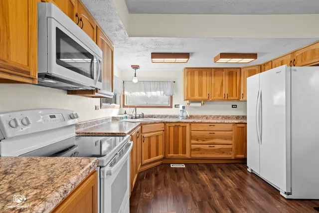 a kitchen with granite countertop a refrigerator a stove a sink and dishwasher with wooden floor