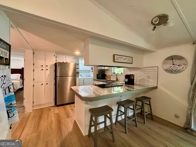 a kitchen with stainless steel appliances a refrigerator a stove a sink a dining table and chairs with wooden floor