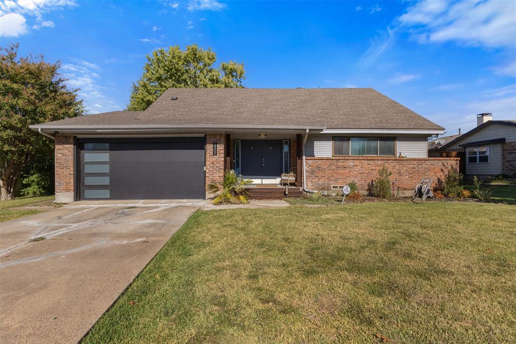 Ranch-style house featuring brick siding, a shingled roof, a front yard, an attached garage, and driveway
