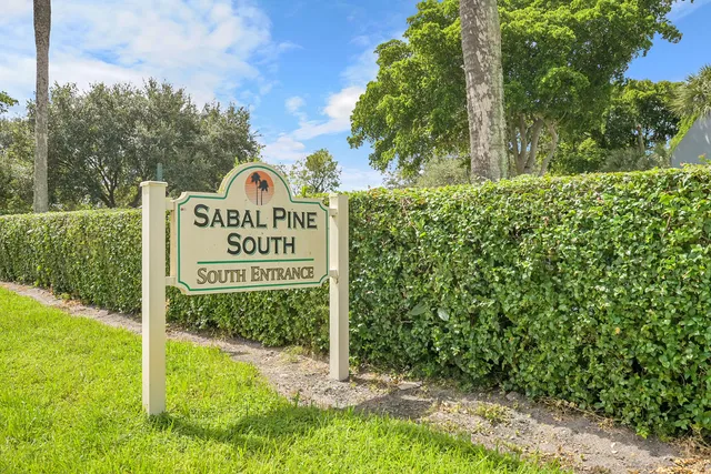 a sign of golf club on a wall under a large tree