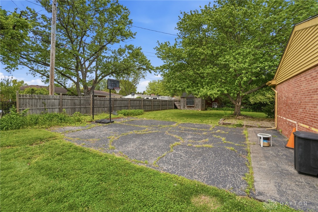 6119 Flemington Road Dayton, OH 45459 - Photo 66 of 76 The expansive yard features a brick facade, mature trees, and a weathered privacy fence.