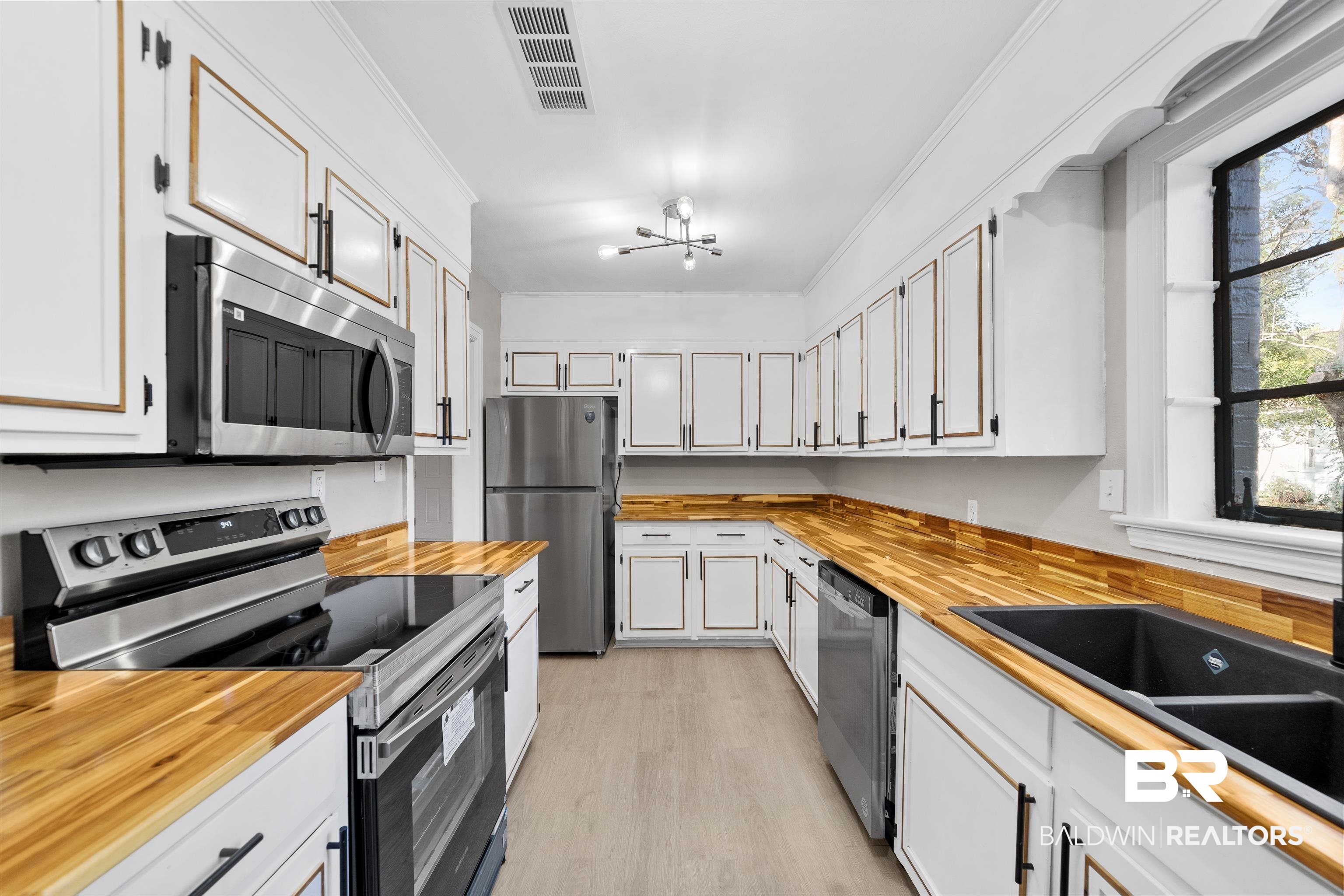 611 Morgan Avenue Mobile, AL 36606 - Photo 13 of 24 Kitchen featuring appliances with stainless steel finishes, light hardwood / wood-style floors, white cabinets, crown molding, and a chandelier