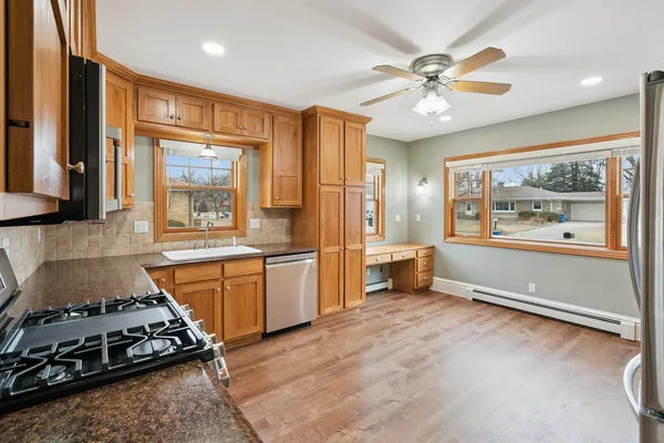 a large kitchen with stainless steel appliances a stove a refrigerator a sink a dining table and chairs with wooden floor