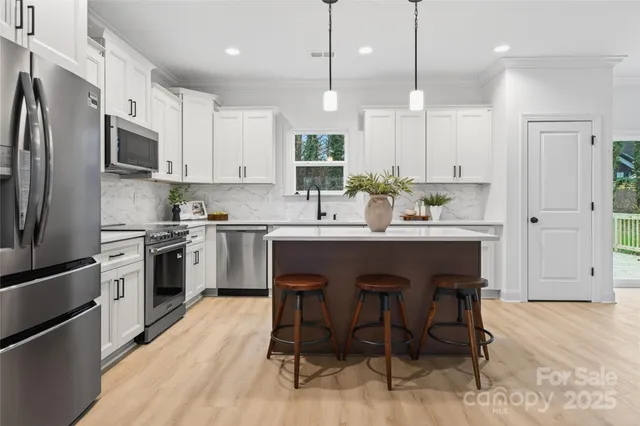 a kitchen with stainless steel appliances kitchen island granite countertop a table chairs refrigerator and microwave