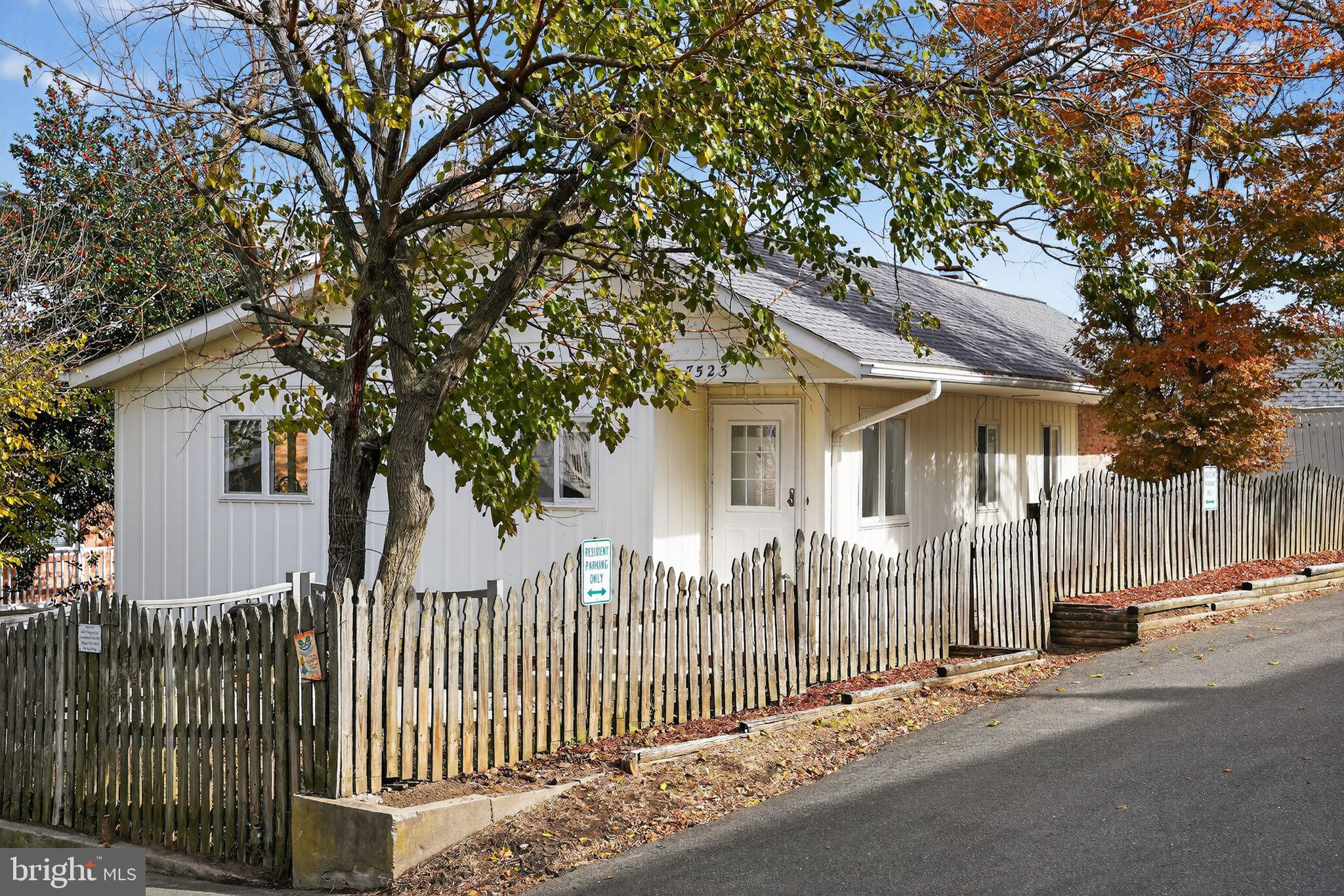 a view of a white house with a large tree and wooden fence